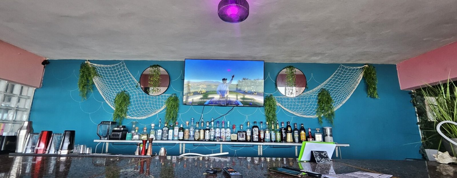 The bar at Selva On The Rocks set up for the evening, with bottles, hanging plants and fishing-net decor